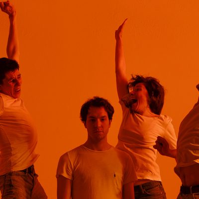 Trois personnes sautent les mains en l'air et une personne est debout, au milieu. La personne debout n'a pas l'air contente.